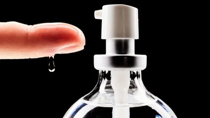 A drop of lubricant on a fingertip beside a pump bottle
