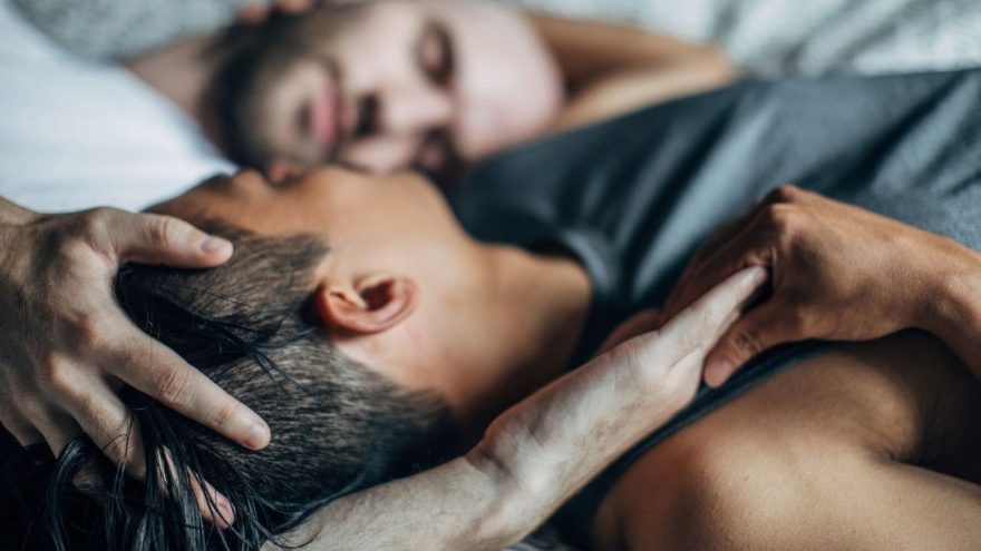 Two men lying together, one cradling the other’s head